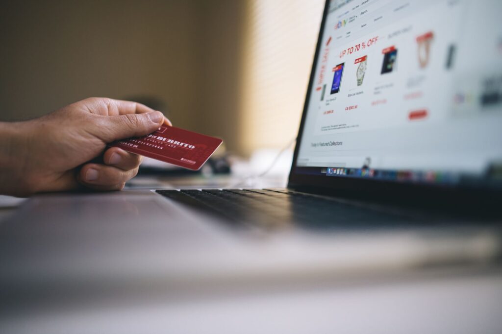 Hand holding a credit card next to a laptop showing an online shop